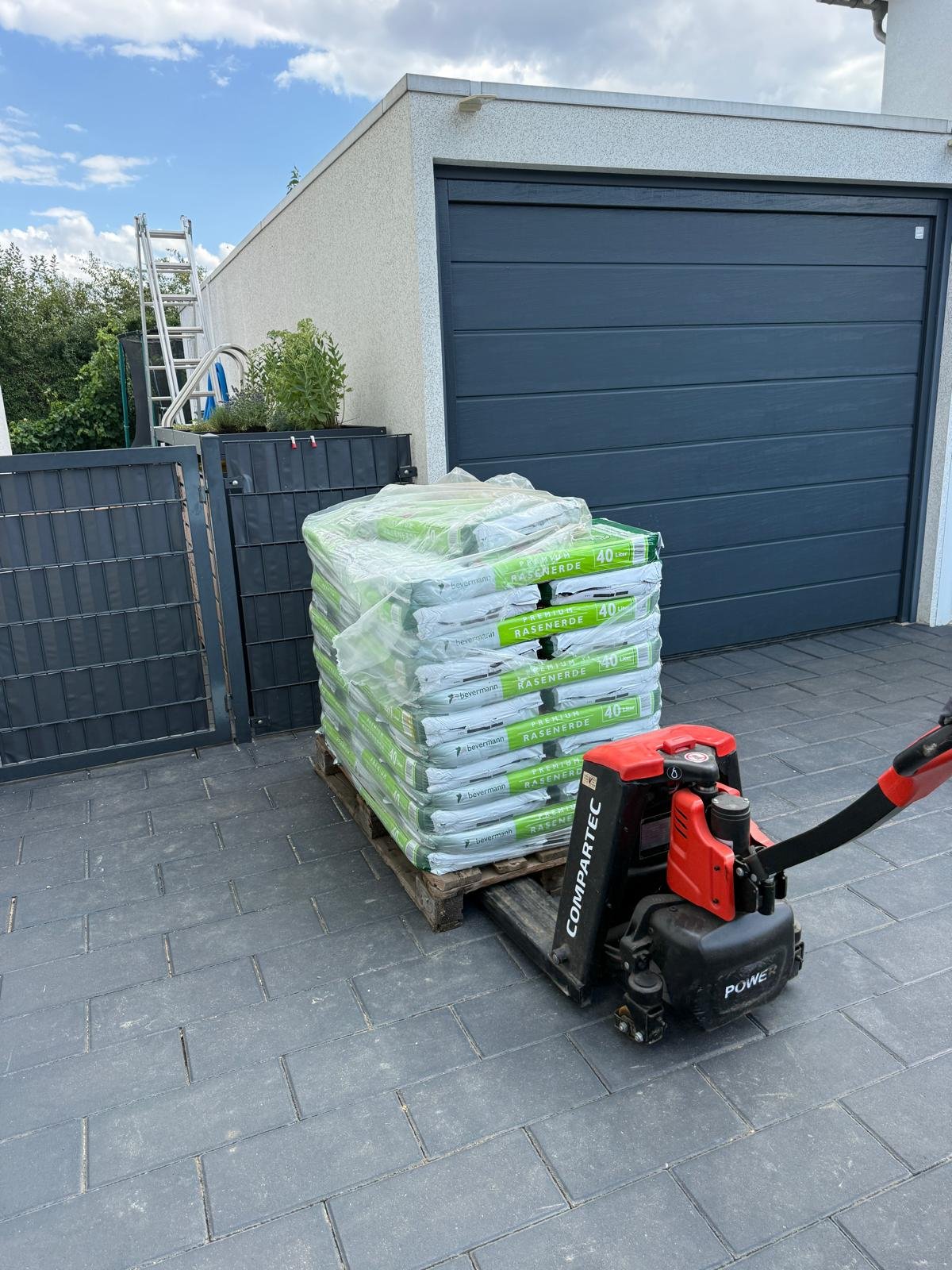 Palette Rasenerde auf Elektrohubwagen direkt vor dem Garagentor einer gepflasterten Einfahrt